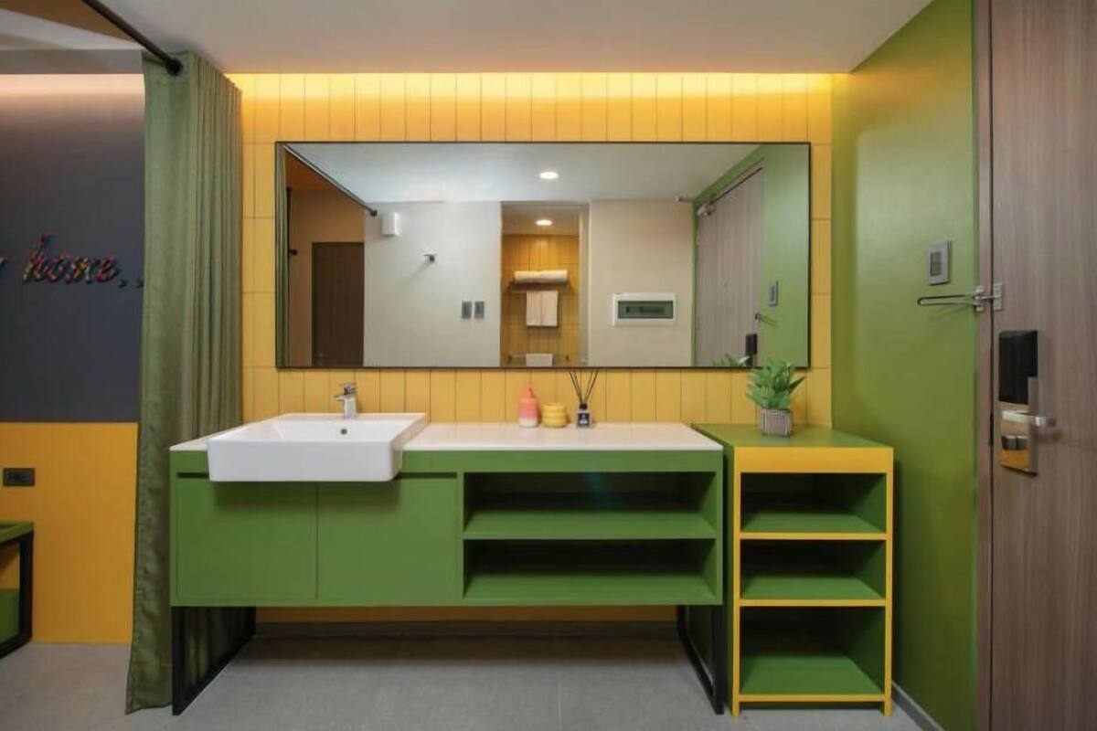 A modern bathroom with a large mirror, a white sink, and green cabinetry.
