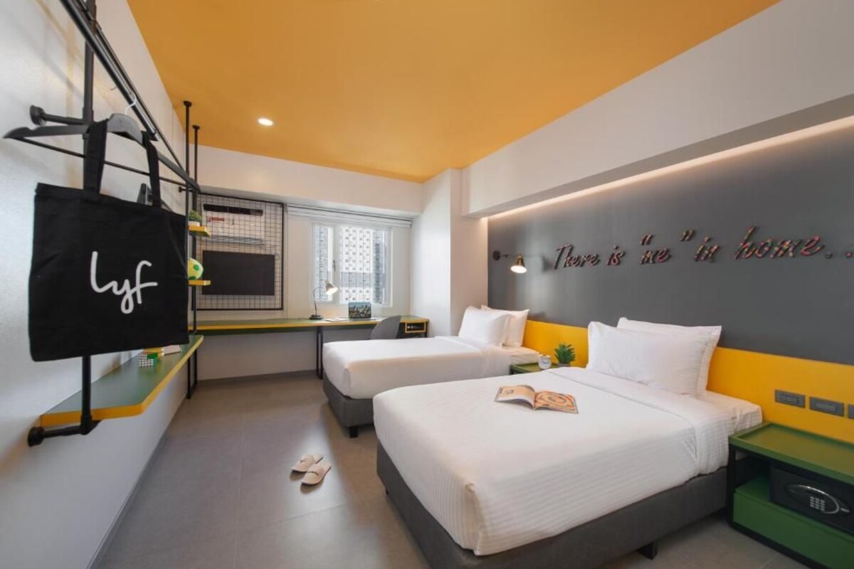 Une chambre d’hôtel avec deux lits, un bureau, une télévision et un mur orné d’une citation inspirante.