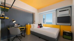 A bedroom with a bed, a desk, a chair, a window, and a TV.