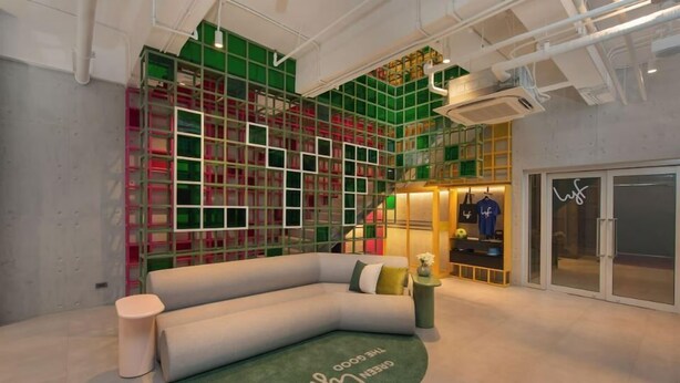 A modern interior with a curved sofa, a small round table, and a green rug with text. - Lyf Malate Manila by Ascott (Manila)