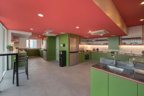 A modern kitchen with green cabinets, a stainless steel refrigerator, and a large island with a sink.