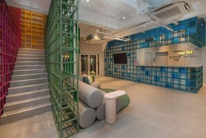 Un intérieur moderne avec un escalier, des sièges modulaires verts et bleus, et un espace d'accueil agrémenté d'une pancarte indiquant « dites bonjour ! ».