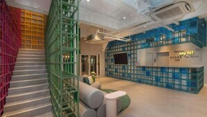 A modern interior with a staircase, green and blue modular seating, and a reception area with a 'say hi!' sign. - Lyf Malate Manila by Ascott (Manila)