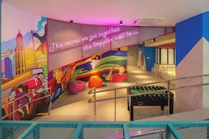Un espacio interior lleno de vida con una mesa de fútbol de mesa, murales coloridos y una cita inspiradora en la pared.