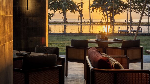 Uma área de estar ao ar livre com móveis de vime e vista para o pôr do sol sobre o oceano.
