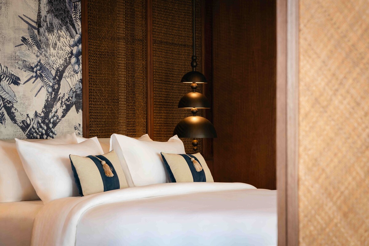 Een hotelkamer met een net opgemaakt bed, een decoratieve muur met een patroon wandtapijt, en een wandlamp.
