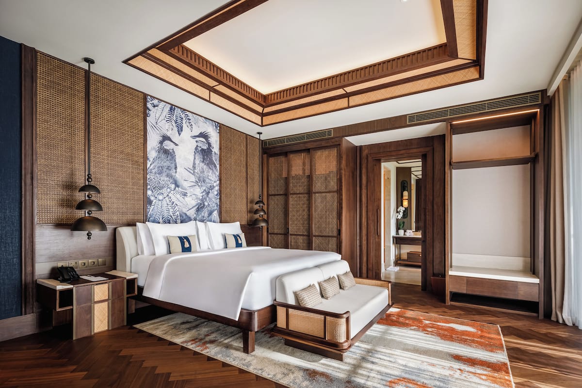 Ein modernes Hotelzimmer mit einem großen Bett, einem Holzkopfende und Blick auf den Flur.