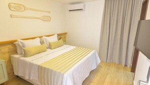 A hotel room with a bed, pillows, a nightstand, an air conditioning unit, and a curtain. - Pousada Topazio (Cairu)