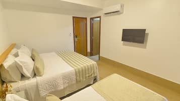 Habitación de hotel con dos camas, cabecero de madera, televisor de pantalla plana y aire acondicionado en la pared.