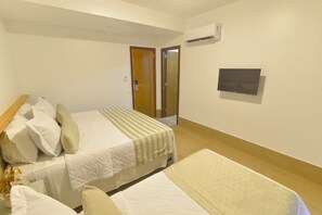 A hotel room with two beds, a wooden headboard, a flat-screen TV, and an air conditioning unit on the wall. - Pousada Topazio (Cairu)