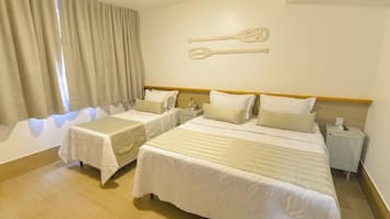 Habitación de hotel con dos camas, una mesita de noche, un reloj en la pared y un ventanal con cortinas.