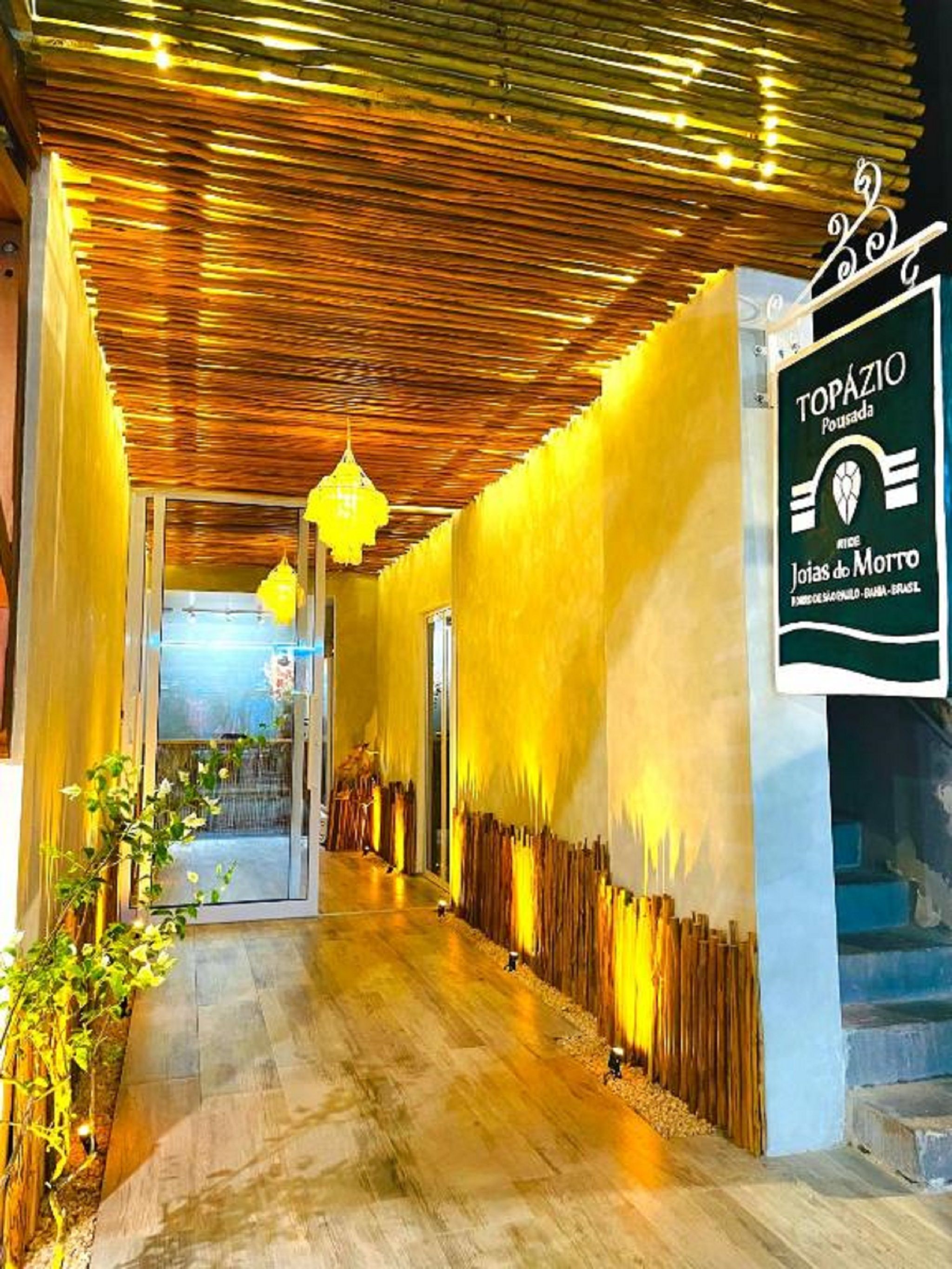 A corridor with a wooden ceiling, yellow walls, and a sign for Topazio Pousada.