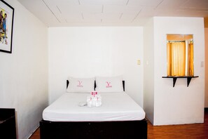 A neatly made bed with white linens and a small table with a red sign, a framed picture on the wall, and a window with curtains. - Victoria Mansions By Zuzu (Manila)