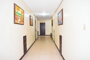 A hallway with framed artwork on the walls, a door at the end, and a tiled floor. - Victoria Mansions By Zuzu (Manila)