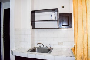 Een keuken met een spoelbak, een plank met een waterkoker en een klein kastje.