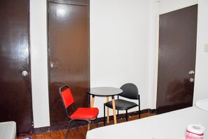 A hotel room with a bed, a small table with two chairs, and two doors.