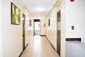 A hotel hallway with doors on both sides, a fire extinguisher, and a sign indicating an exit. - Victoria Mansions By Zuzu (Manila)