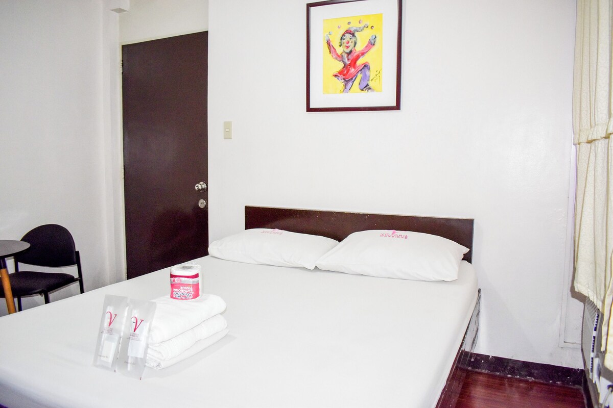 A hotel room with a bed, a chair, a painting on the wall, and a door.