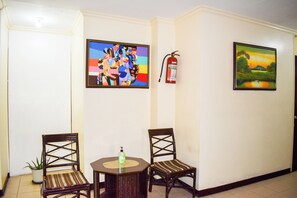 A room with two wooden chairs, a small table, a potted plant, and two framed paintings on the walls. - Victoria Mansions By Zuzu (Manila)