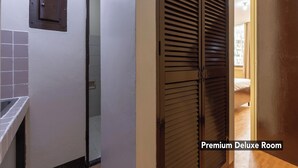A hallway leading to a room with a sliding door, a tiled wall, and a visible bed in the adjacent room.