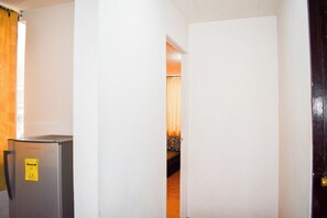 A hallway with a refrigerator on the left, a door on the right, and a bed in the background. - Victoria Mansions By Zuzu (Manila)