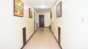 A hallway with framed artwork on the walls, a door at the end, and a tiled floor.