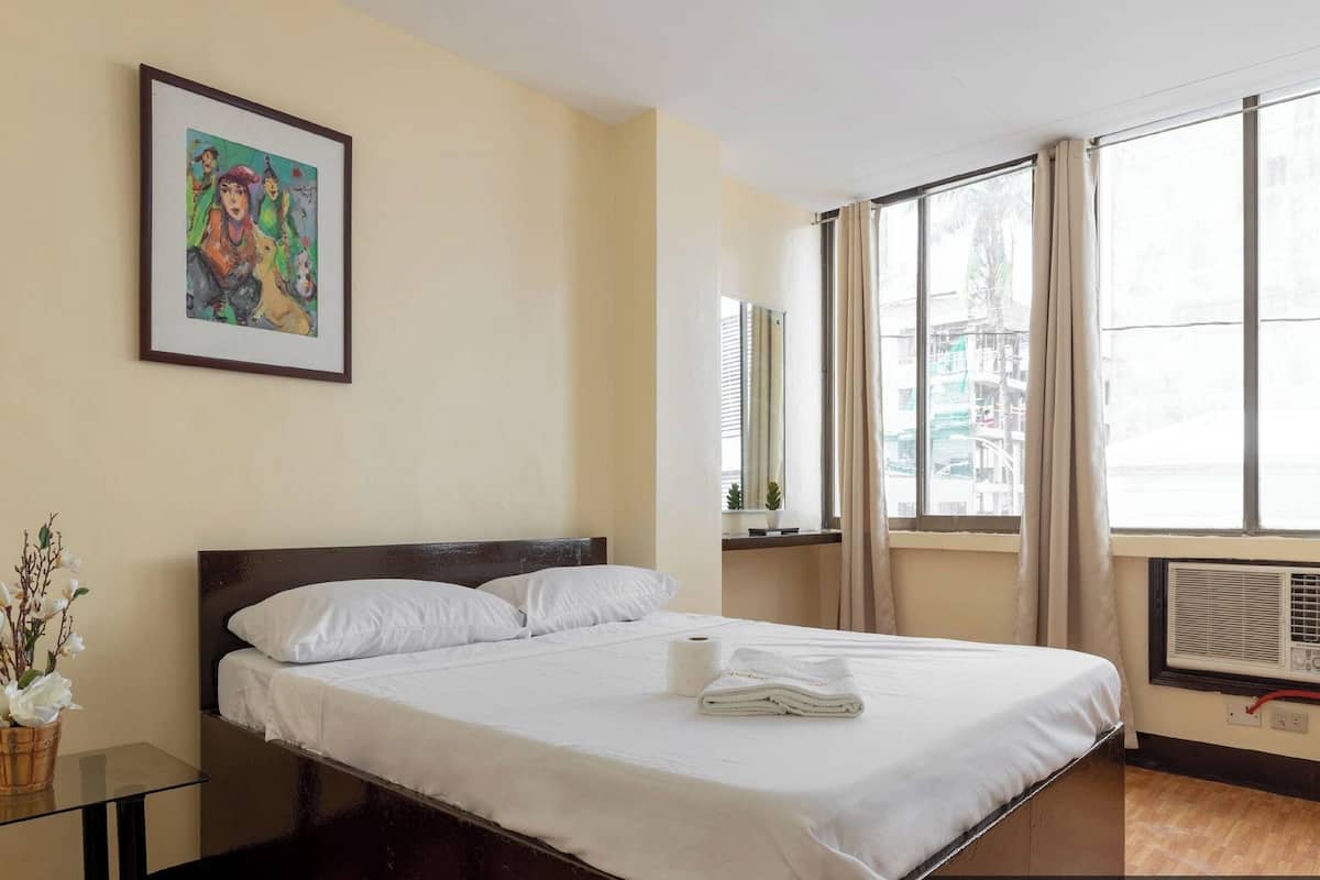 Una habitación de hotel con una cama, un cuadro enmarcado, una ventana con cortinas y un radiador.