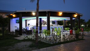 Un restaurante al aire libre con zona de estar techada, mesas y sillas.