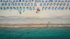 A beach with rows of blue umbrellas and lounge chairs, a sandy shore, and a clear blue sea. - Club Esse Aquilia Beach Village (Badolato)