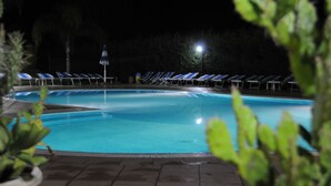 Una piscina con sillas reclinables azules y un poste de luz por la noche.