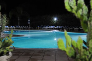 Una piscina con sillas reclinables azules y un poste de luz por la noche.