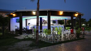 Un restaurante al aire libre con zona de estar techada, mesas y sillas.