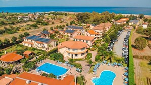 Un resort con varias edificaciones, una piscina y una zona de playa con tumbonas.