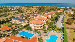 Un resort con varias edificaciones, una piscina y una zona de playa con tumbonas.