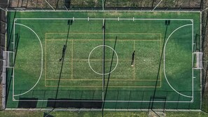 Vista aérea de un campo deportivo con zonas delimitadas para fútbol y baloncesto, rodeado por una valla.