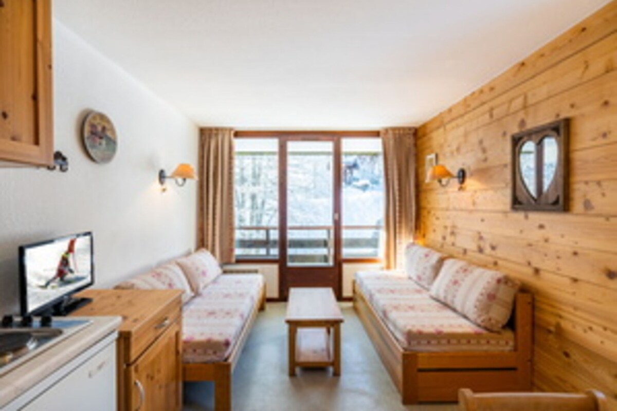 Una habitación con interior de madera, un sofá, una mesita y un televisor.