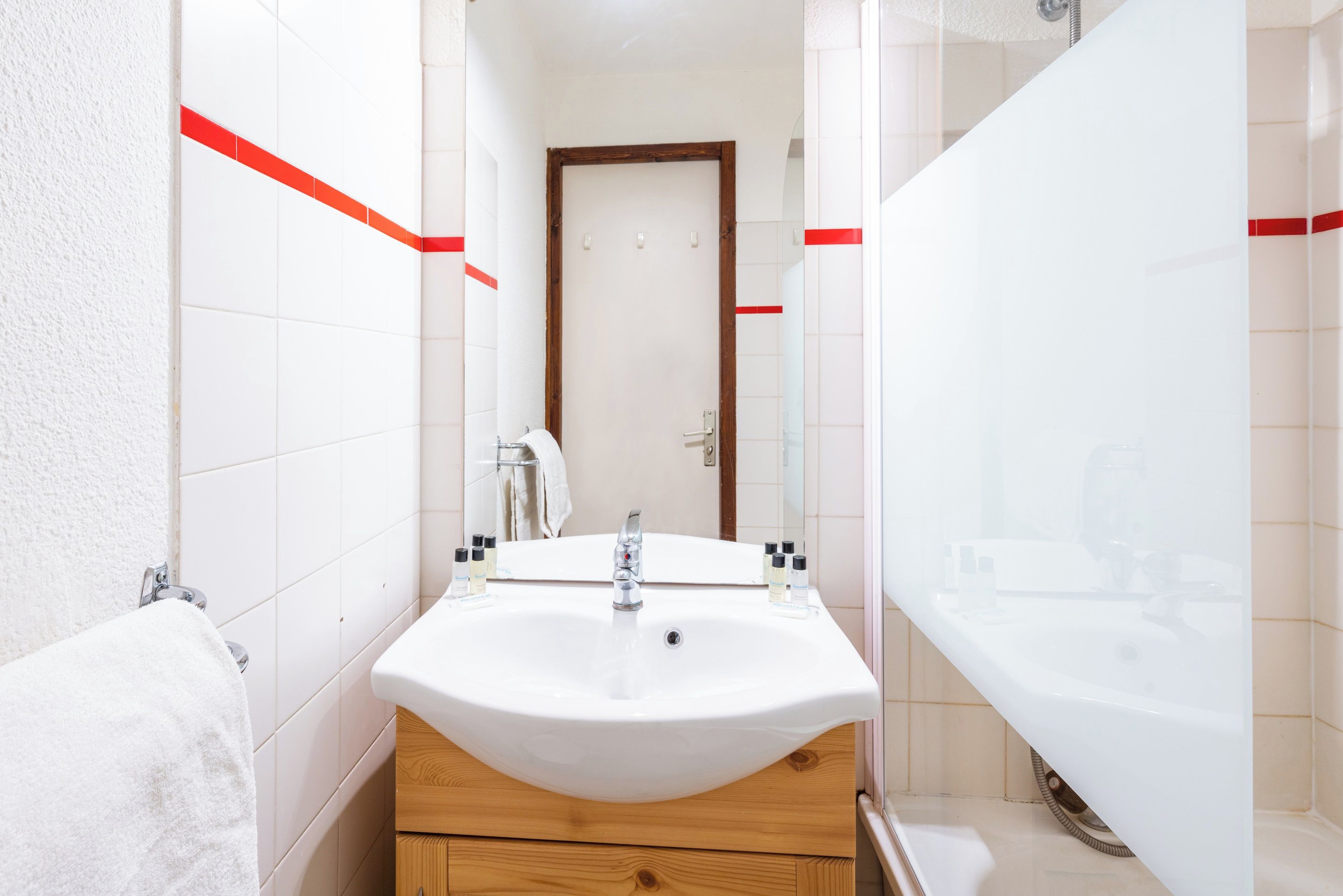 Un baño con lavamanos blanco, tocador de madera y cabina de ducha de vidrio.