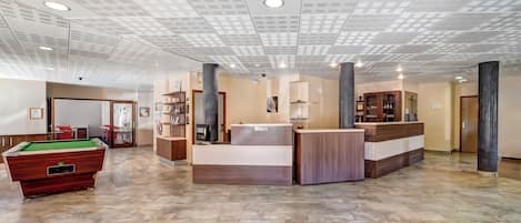 Un hall amplio con mesa de billar, mostrador de recepción y un diseño de techo moderno.