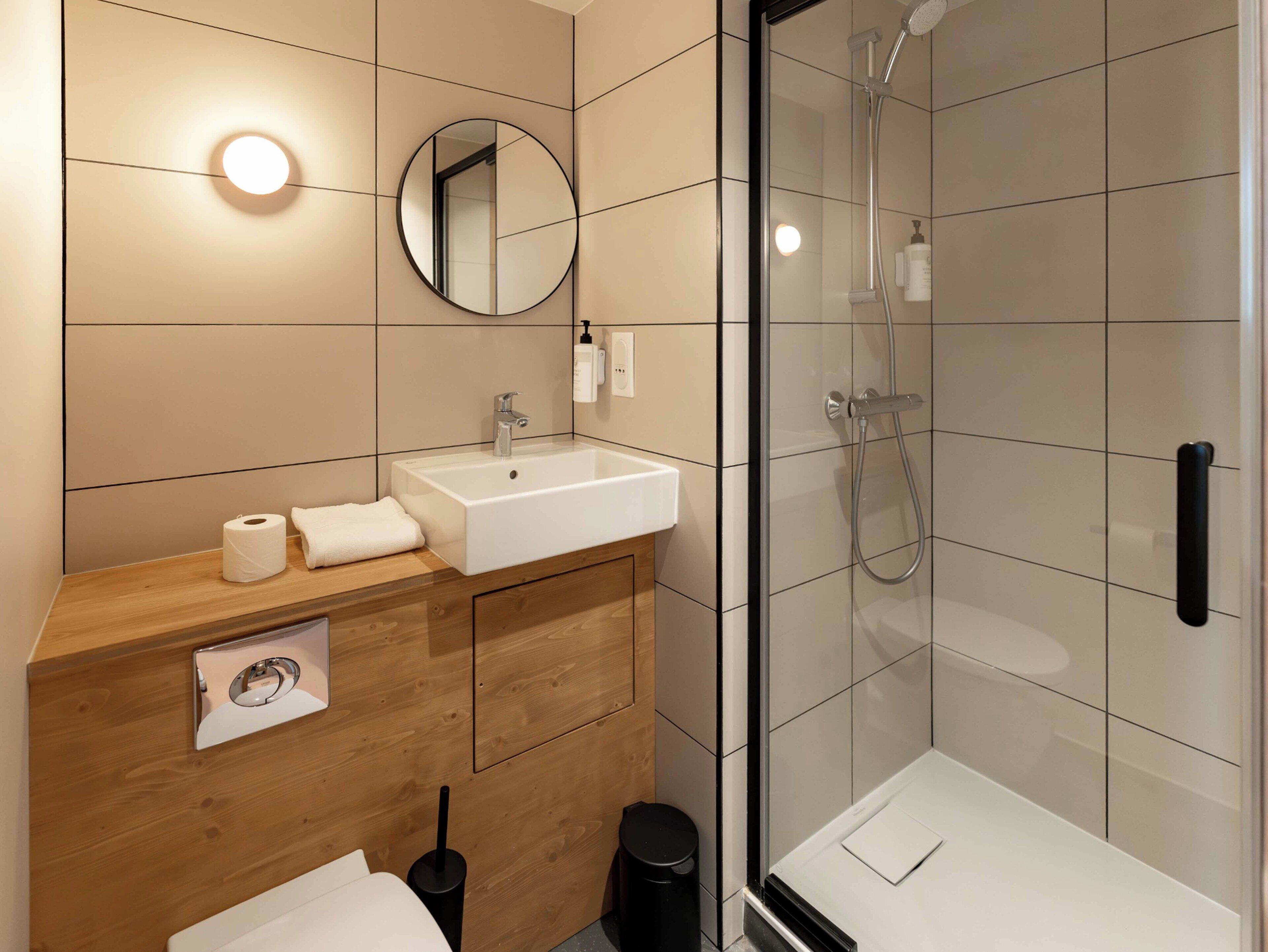 A modern bathroom with a wooden vanity, a white sink, a mirror, and a glass-enclosed shower.