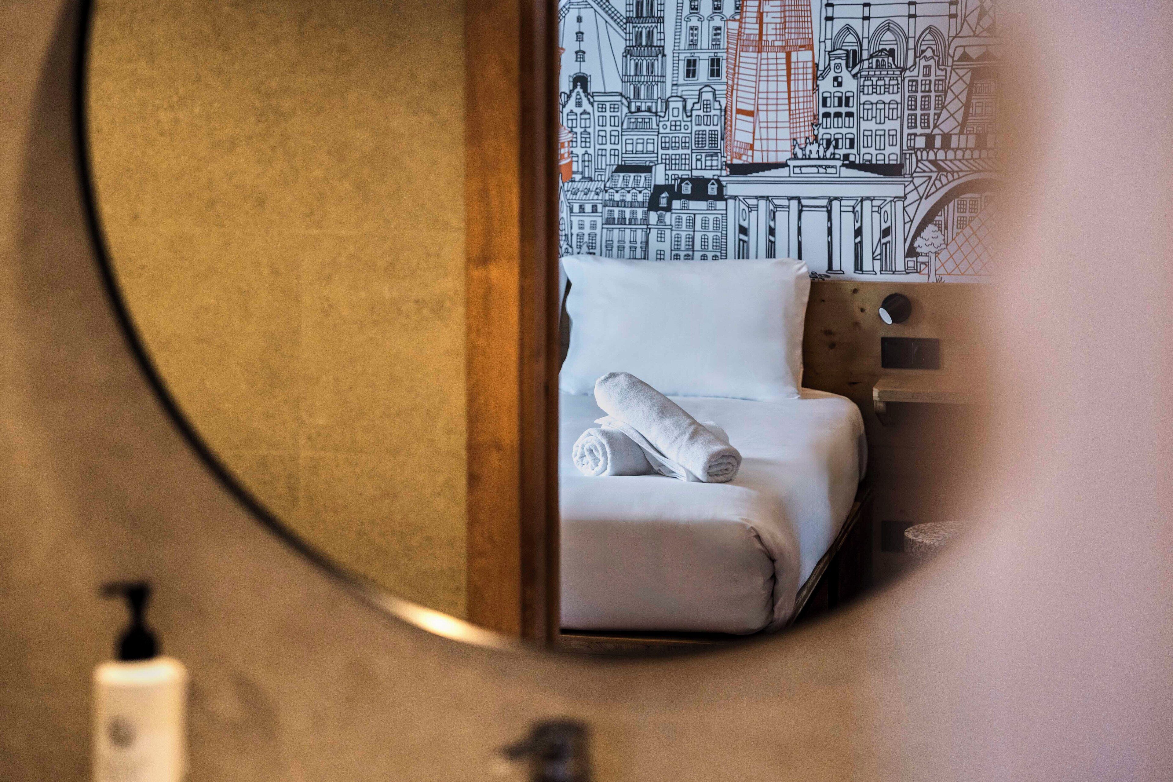 Une salle de bain avec un miroir rond, une serviette blanche et un lit avec un oreiller blanc.