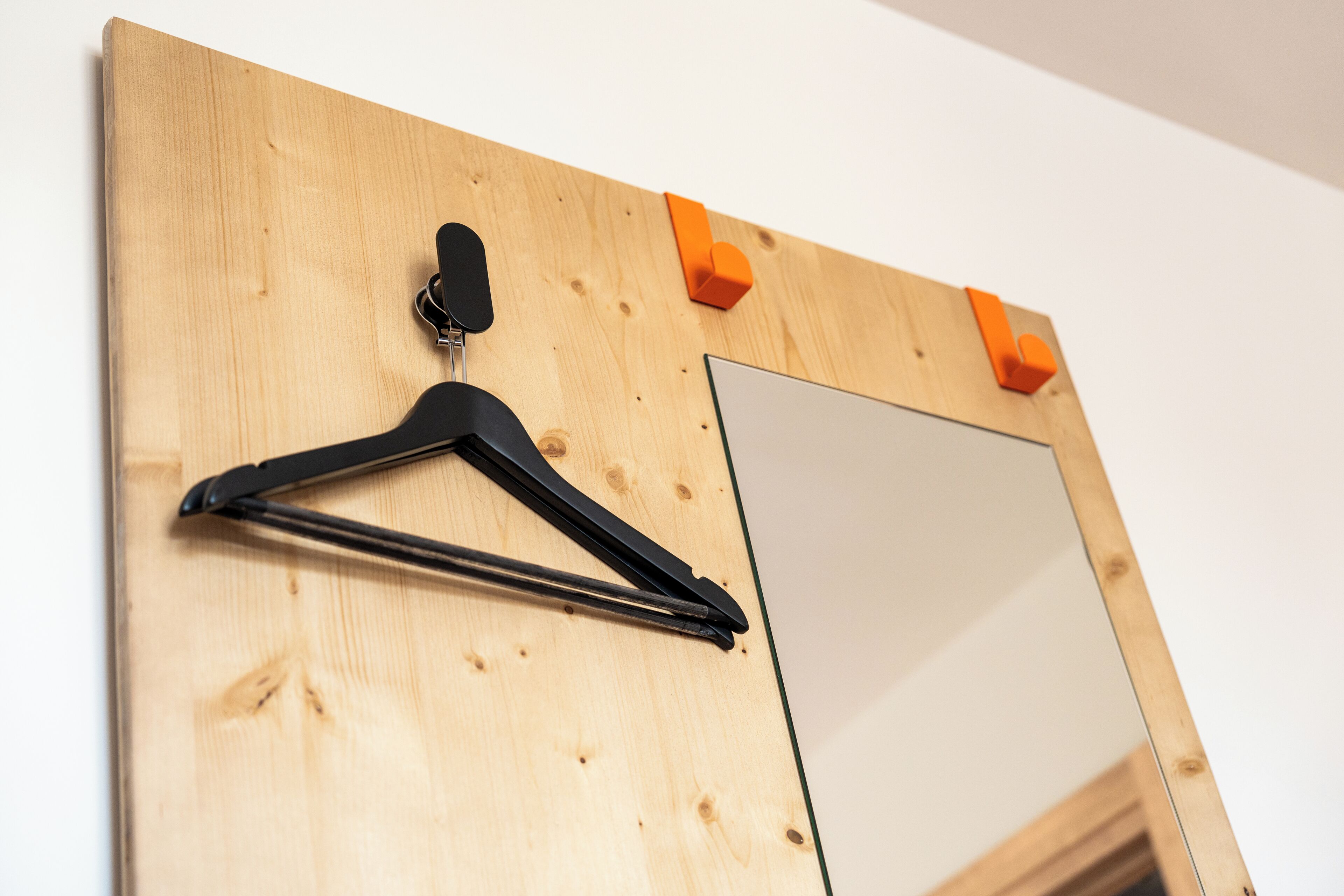 A wooden wall with a black hanger and two orange clips.