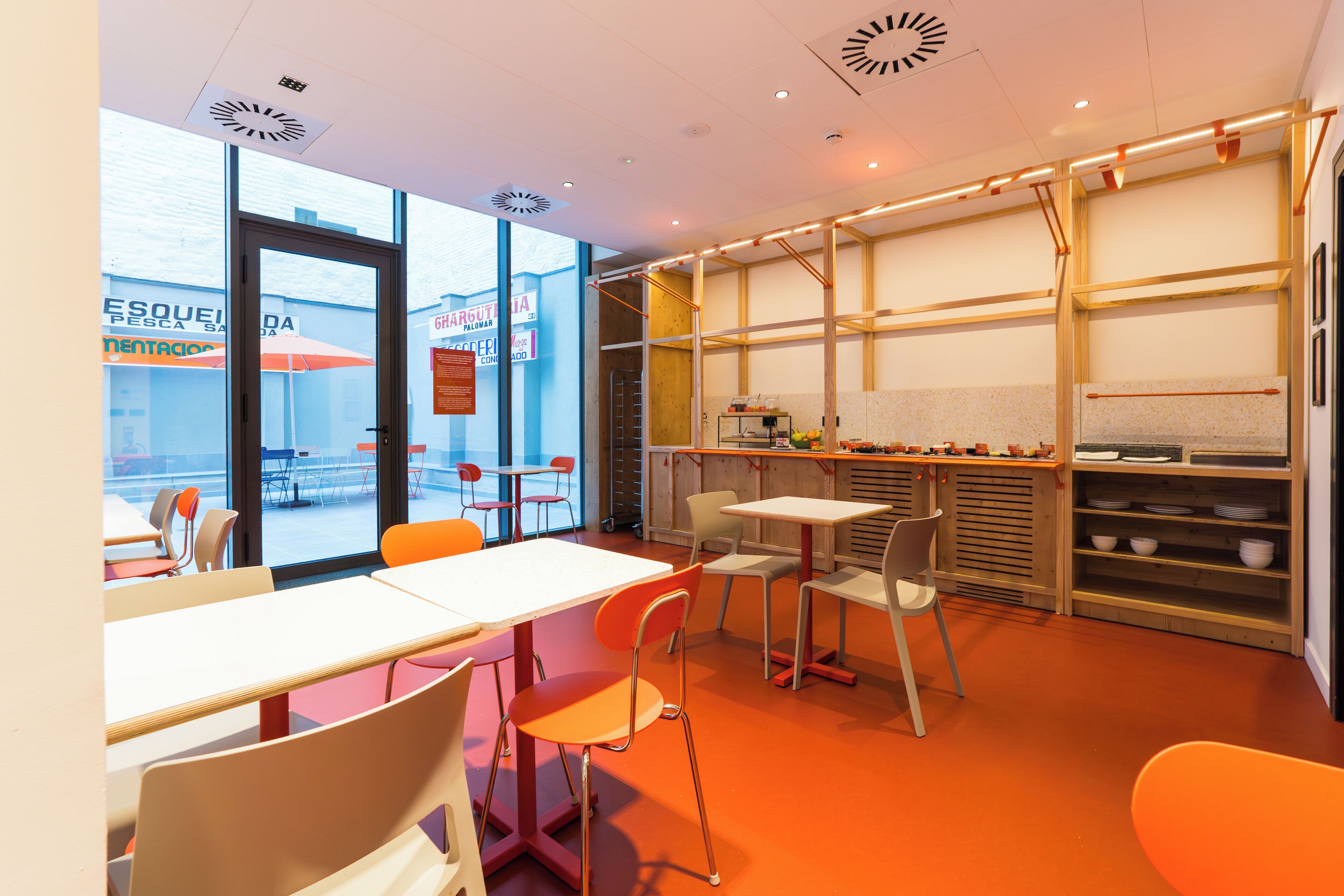 Un interior moderno con mesas, sillas, una zona de cocina y ventanas amplias.
