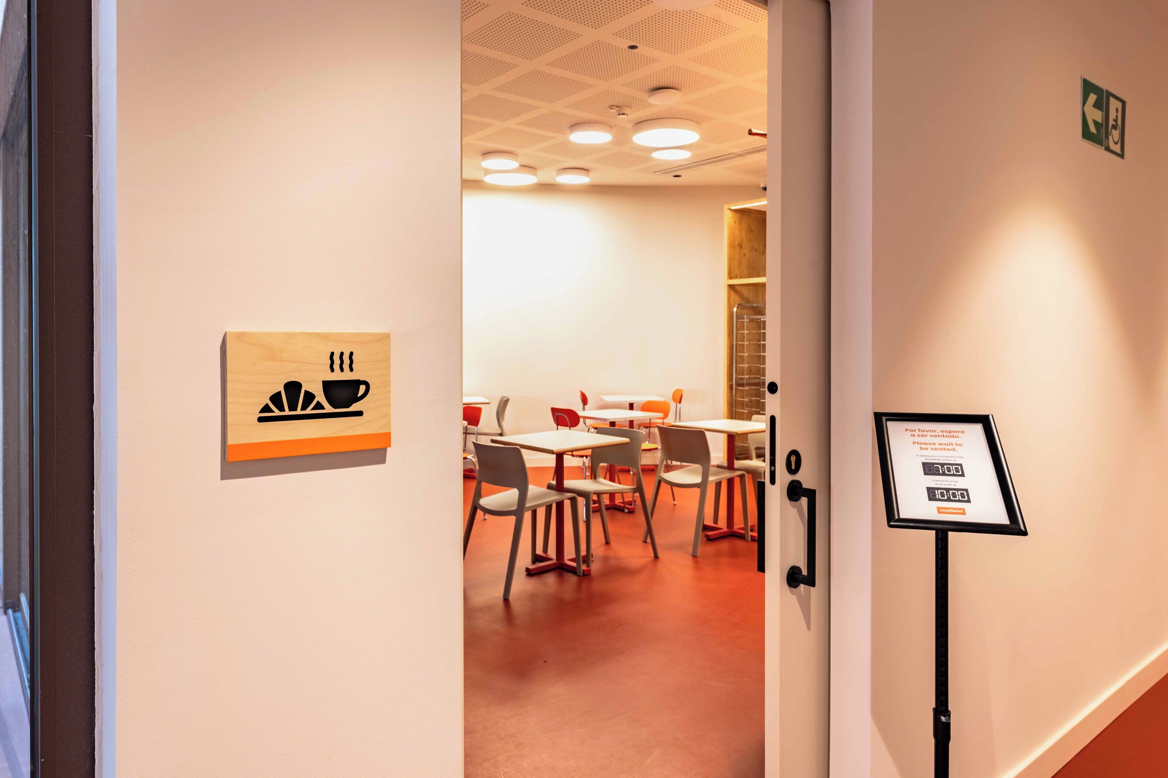 Un hall d’hôtel avec un panneau en bois, une horloge numérique et un panneau indiquant que l’établissement est accessible aux personnes à mobilité réduite.
