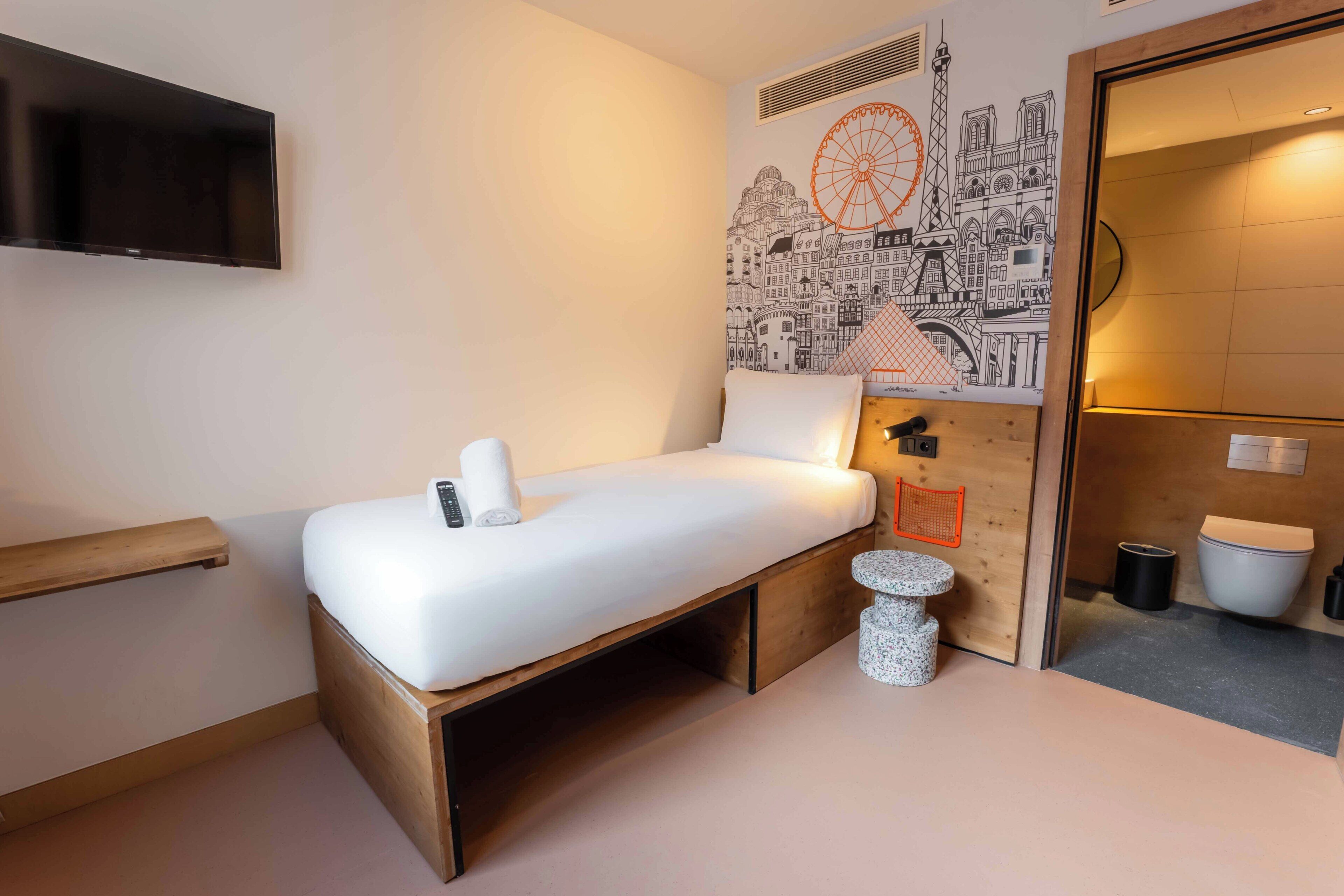 Ein Schlafzimmer mit einem Bett, einem Fernseher, einem kleinen Tisch und einem durchgegangenen Tür sichtbaren Badezimmer.