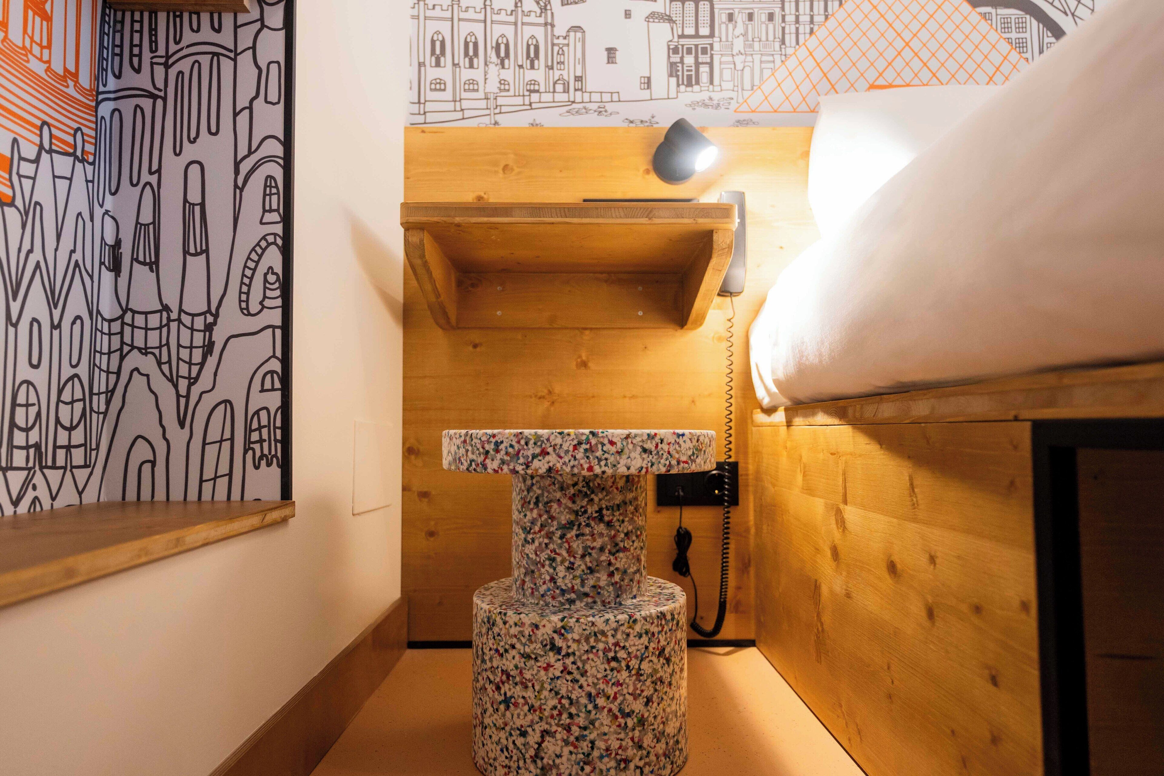 Une petite pièce avec un lit en bois, un arbre à chat et un téléphone fixé au mur.
