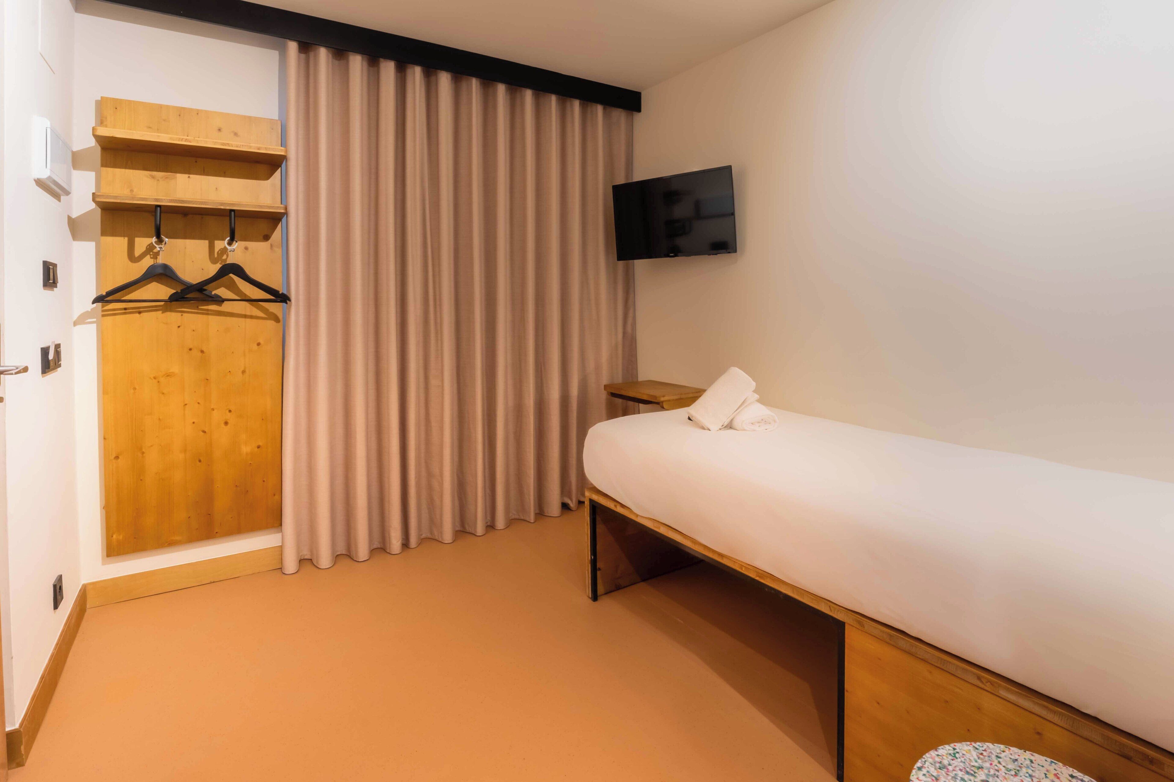 Una habitación de hotel con una cama, un armario de madera, un televisor y una cortina.