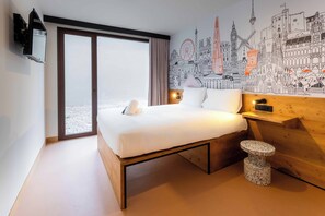 Un hotel moderno con una cama grande, una mesita de noche de madera, una pequeña mesa redonda y un mural con vistas a la ciudad en la pared.