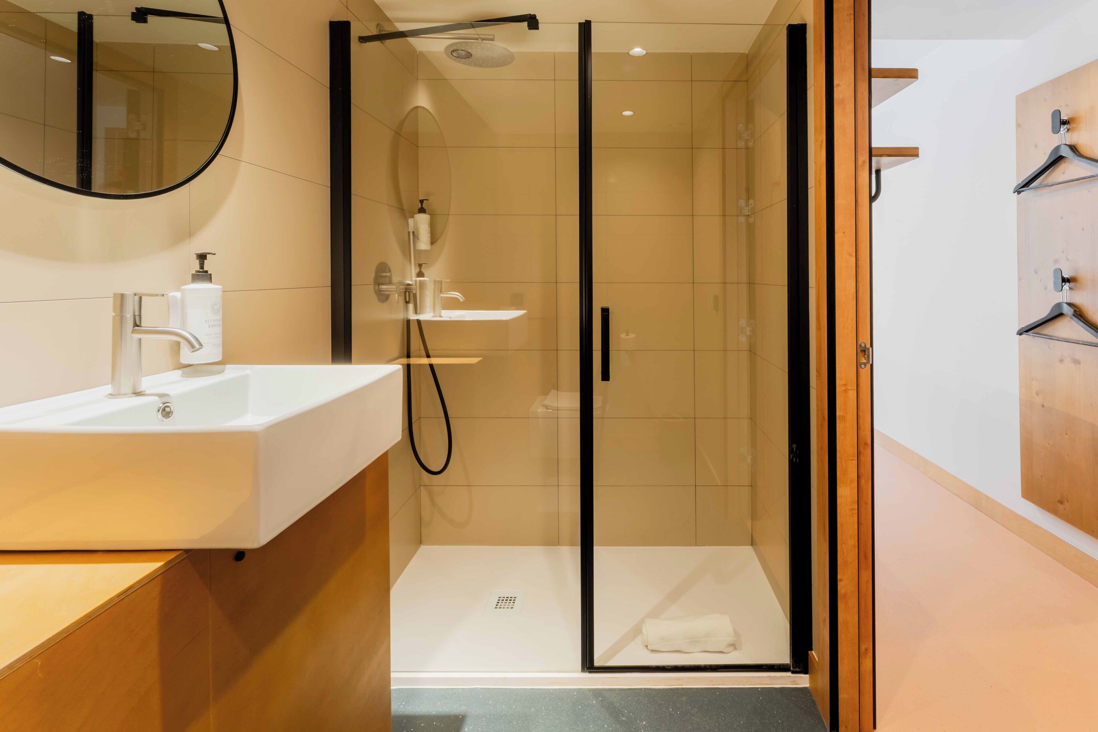 Une salle de bain moderne avec une douche à parois de verre, un lavabo blanc doté d’un distributeur de savon et un meuble-lavabo en bois.