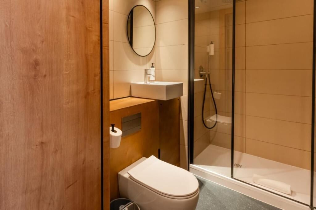 Een moderne badkamer met een houten wastafelmeubel, toilet, glazen douchecabine en spiegel.