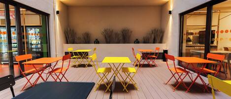 An outdoor seating area with tables and chairs, a wooden deck, and a wall with plants.